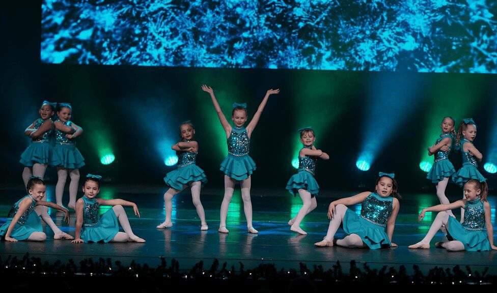 Teal-costumed children performing synchronized dance