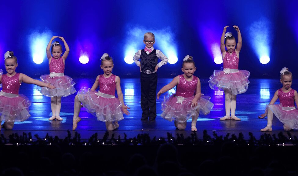 Little boy in vest surrounded by pink tutus