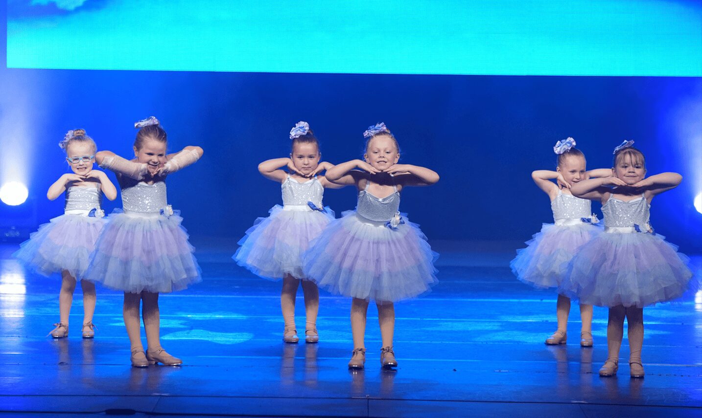 Six little ballerinas posing under blue lights